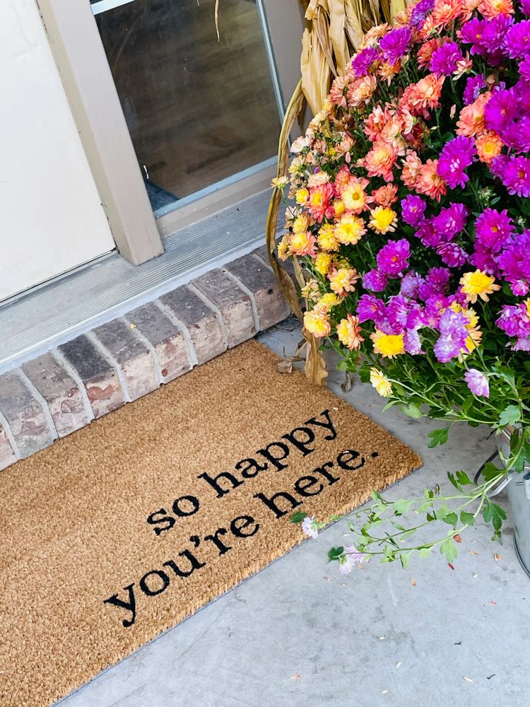 Welcome mat with cheerful message and colorful flowers at a doorstep.