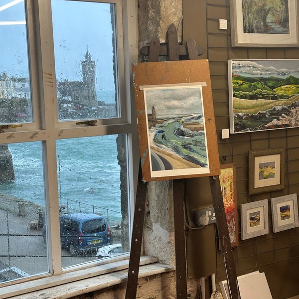 Painting on an easel beside a rainy window overlooking a coastal town.