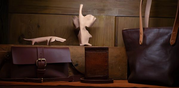 Handcrafted leather bags and wallets displayed on a wooden shelf with artistic clay sculptures.