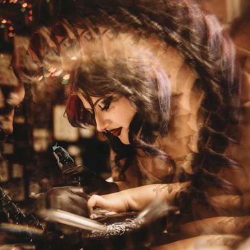 A woman with dark hair and makeup is writing or drawing, captured with a kaleidoscopic effect.