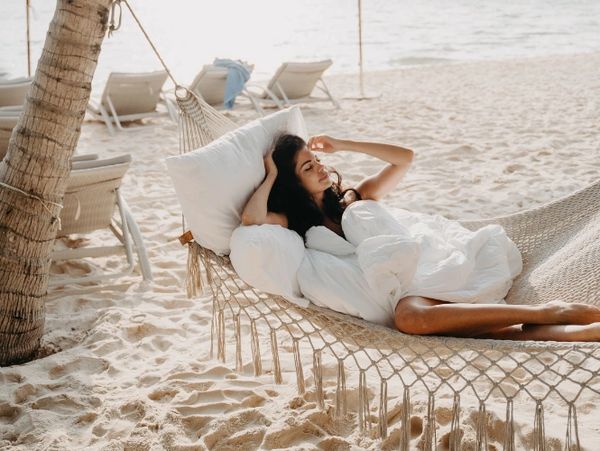 a brunette lady relaxing in a hammock on a beach with a white sheet