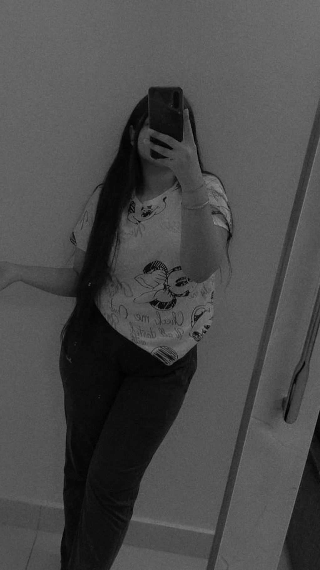 A person taking a mirror selfie in casual wear with a long hairstyle.