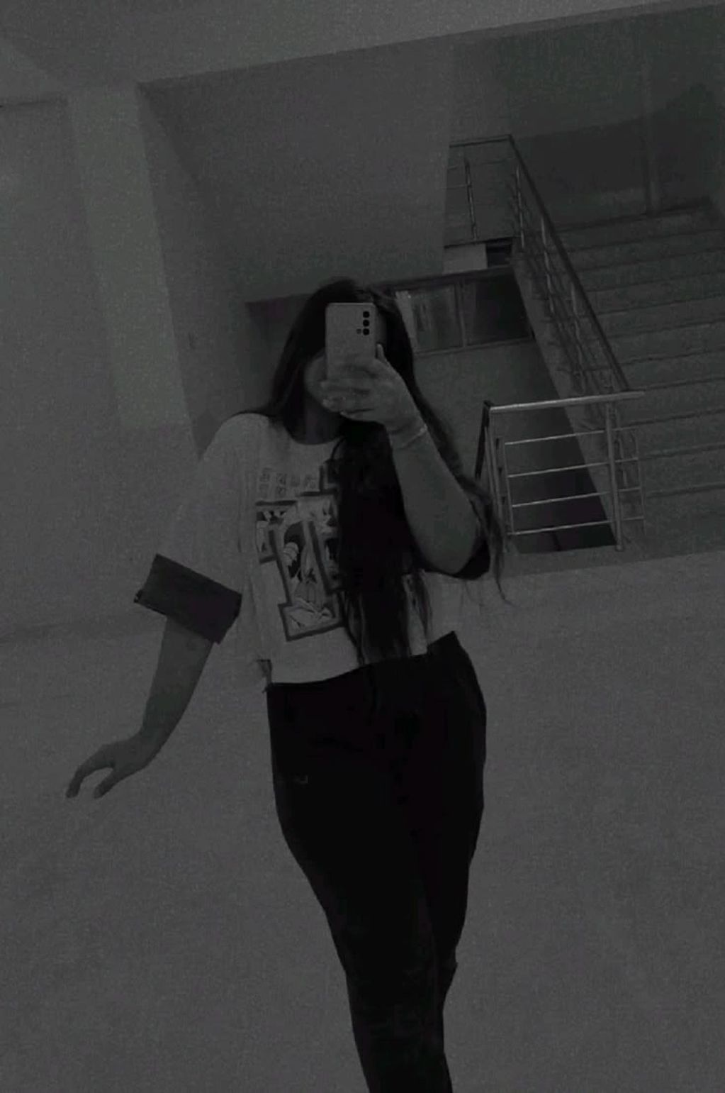 Person taking a mirror selfie in a dimly lit stairwell wearing a graphic t-shirt.