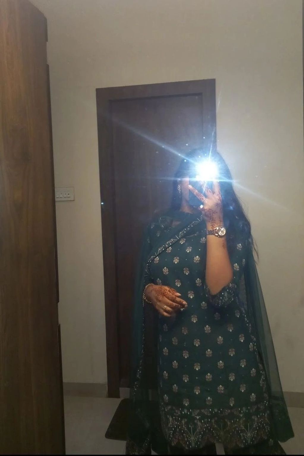 Woman in traditional attire taking a mirror selfie with flash obscuring her face.