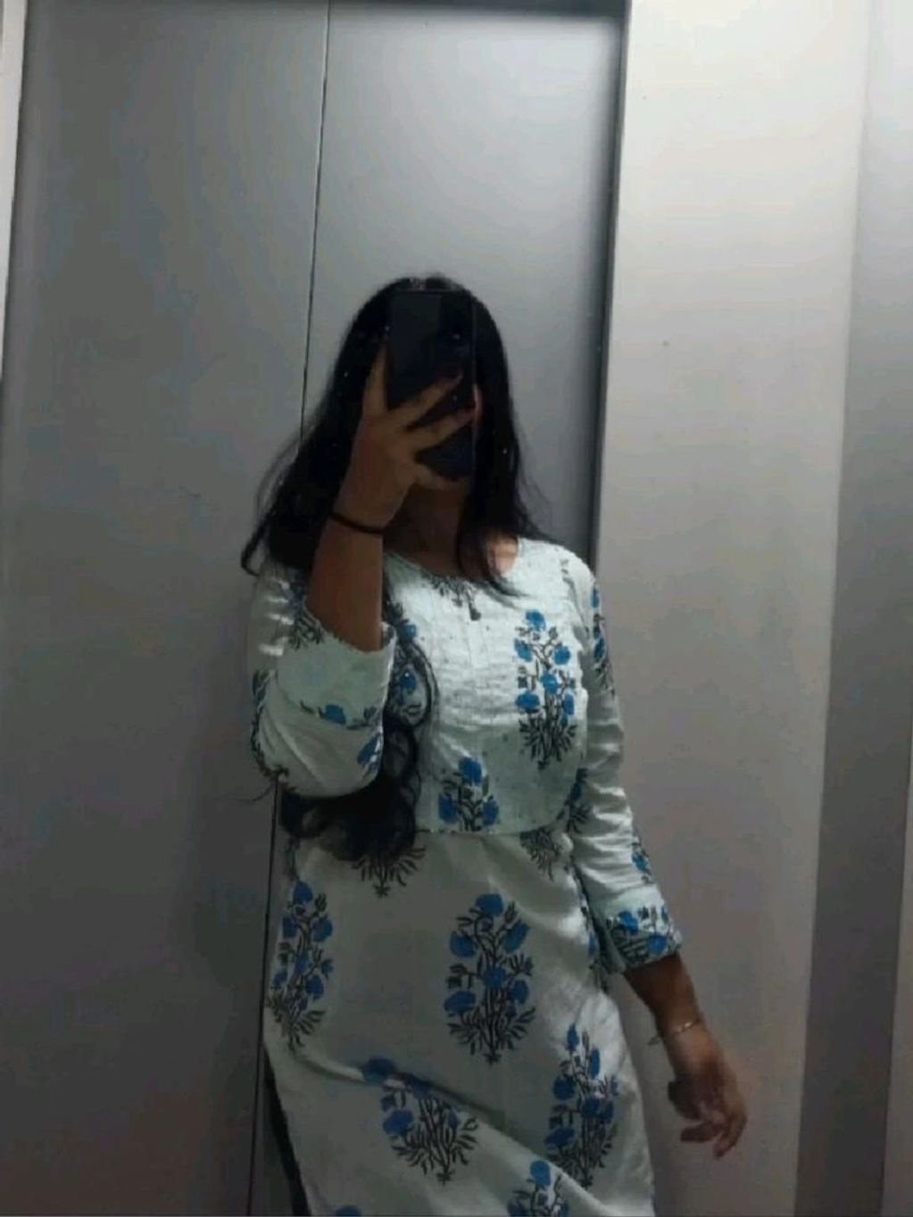 Woman taking a mirror selfie wearing a white dress with blue floral patterns.