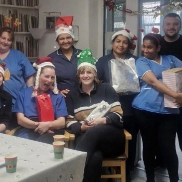 Group of people in festive hats holding gifts and smiling indoors.