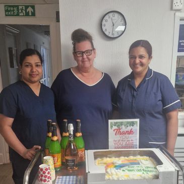Three healthcare workers with cakes and a thank you sign in a hospital setting.