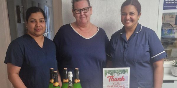 Three healthcare workers posing with champagne bottles and a thank you card.
