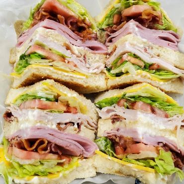Club sandwiches with layers of ham, turkey bacon, lettuce, tomato, mayo and cheese.
