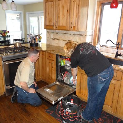 Nutterman's repairman Nick kneeling in front of open Kitchenaid dishwasher in Olathe advising woman