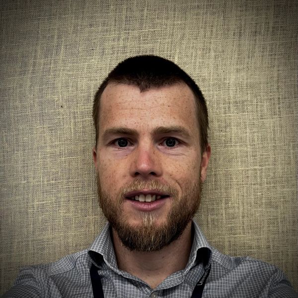 Smiling man with a beard against a textured beige backdrop.