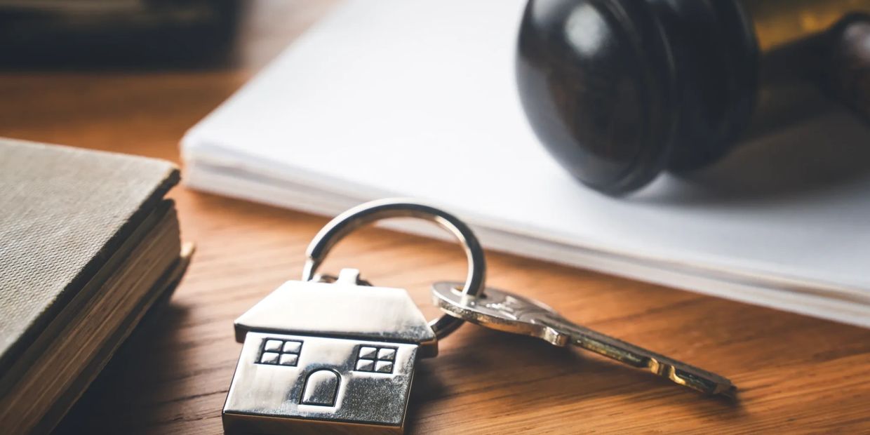 A house-shaped keychain and a key on a wooden table with a judge's gavel in the background.