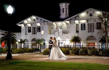 Newlyweds embrace at night in front of a beautifully lit historic building.