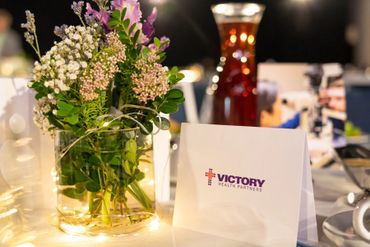 A floral centerpiece and a Victory Health Partners card on a table at a formal event.