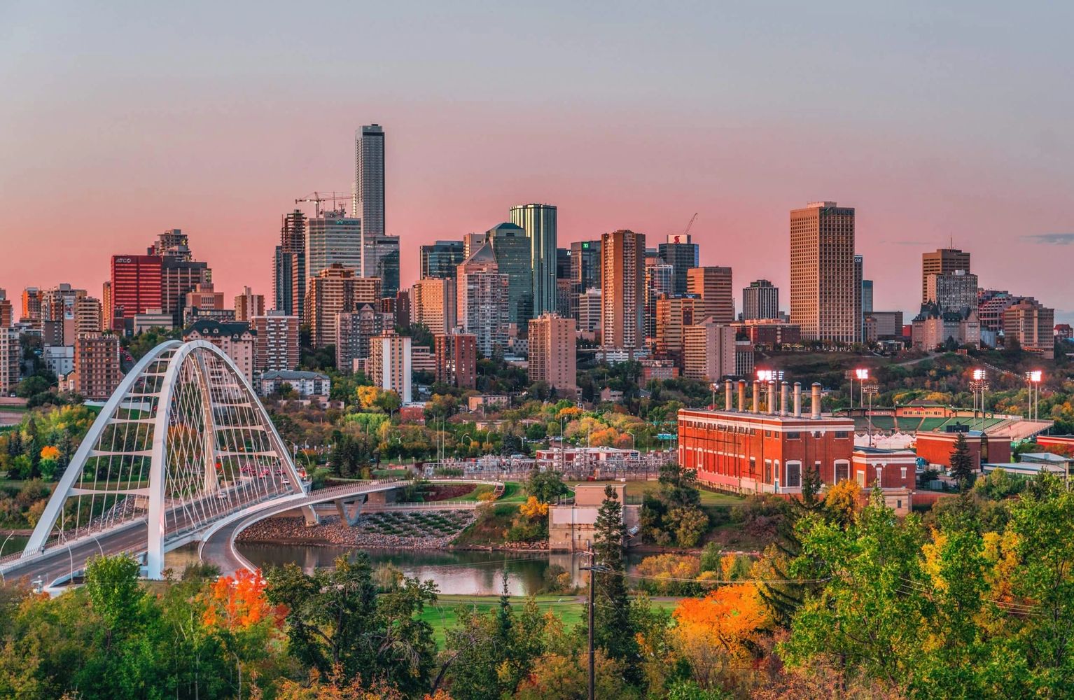 City skyline with a modern bridge and autumn foliage at sunset.