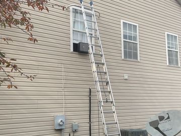 Two ladders leaning against a house near windows.