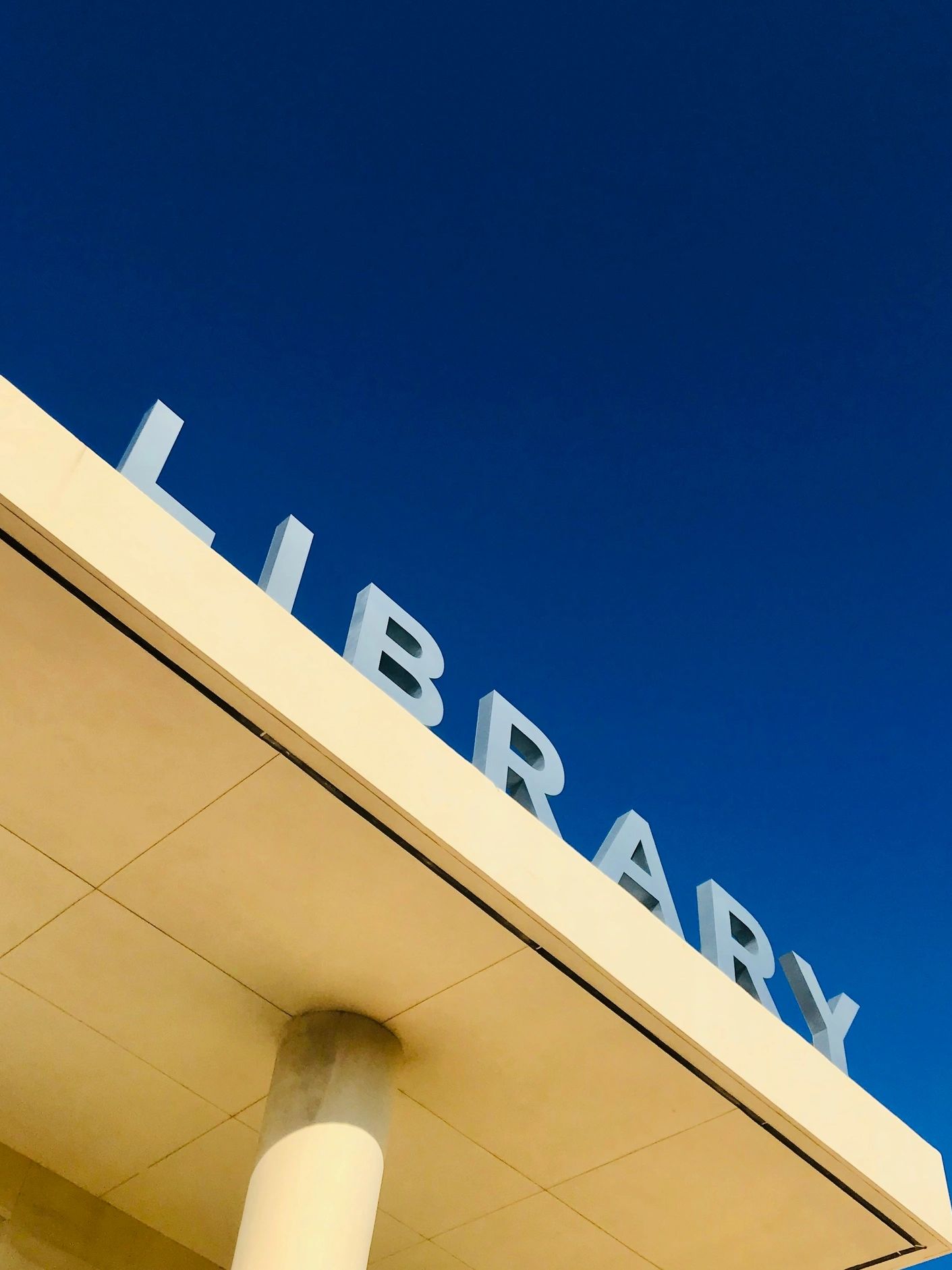 Modern library building with large letters against a clear blue sky.