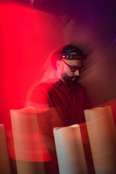 A DJ with headphones immersed in red lighting and smoke effects.