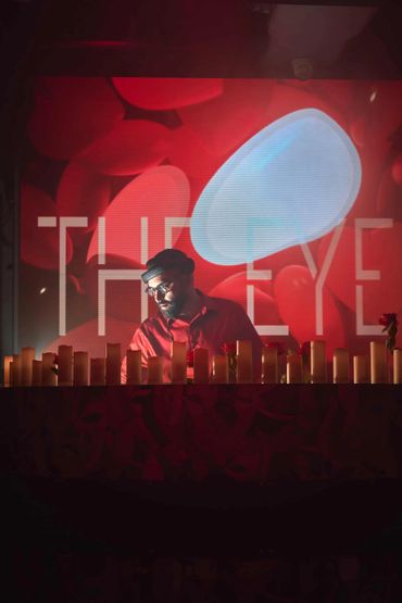 DJ performing with red and blue abstract background and candles in foreground.