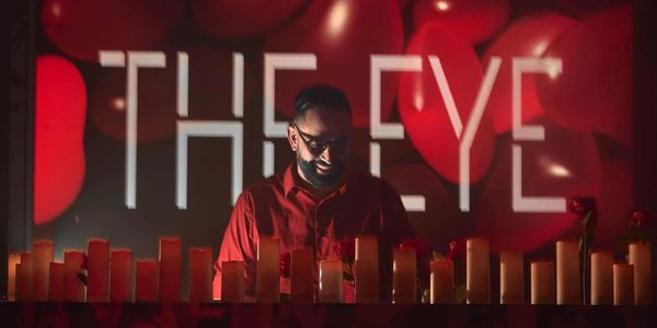 Man smiling behind candles with "THE EYE" in background.