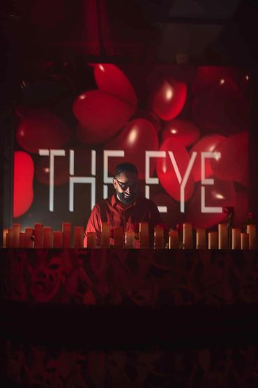 Man smiling behind candles with "THE EYE" in background.