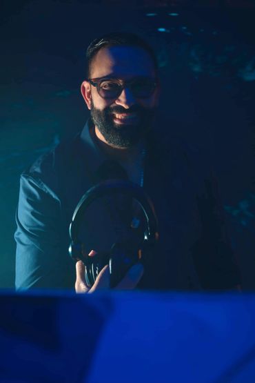 Smiling man holding headphones in low blue lighting.