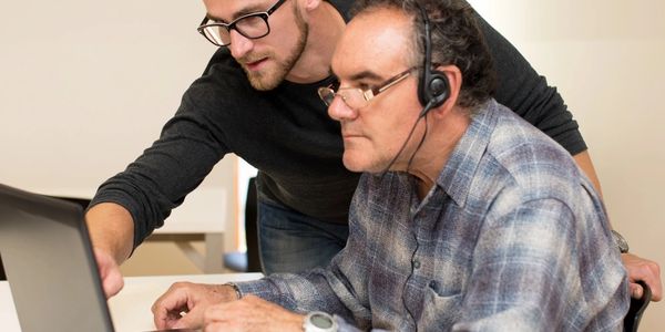 Younger man teaching older man on laptop.