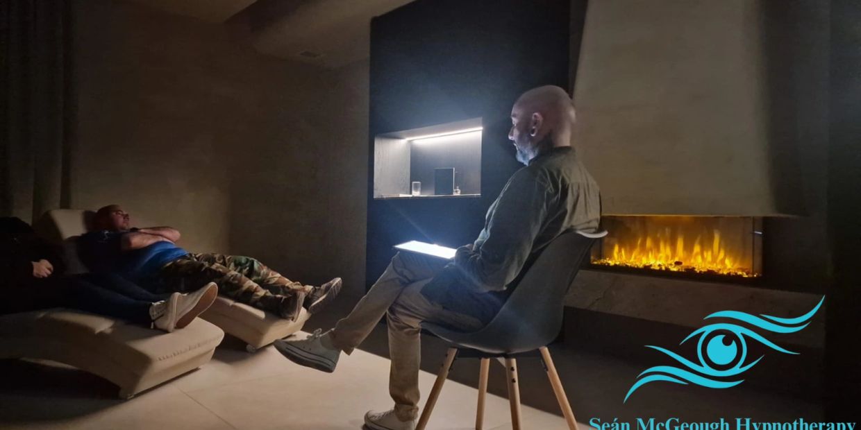 A man reading near a fireplace with others relaxing on lounge chairs.