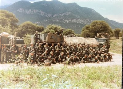 Military group poses with armored vehicle in mountainous area.