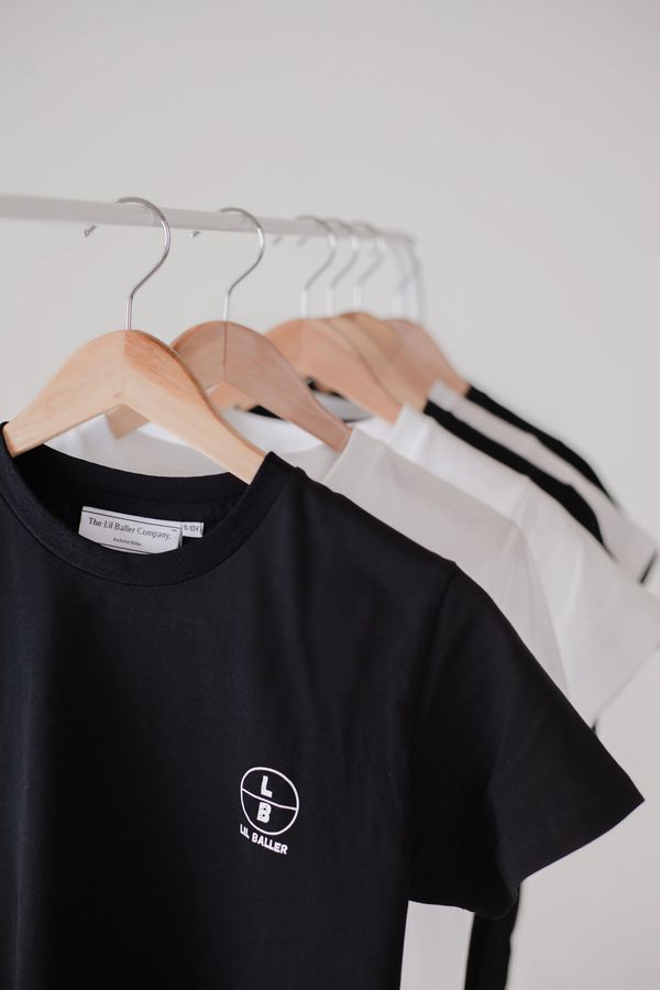 Black and white t-shirts hanging on wooden hangers in a minimalist setting.
