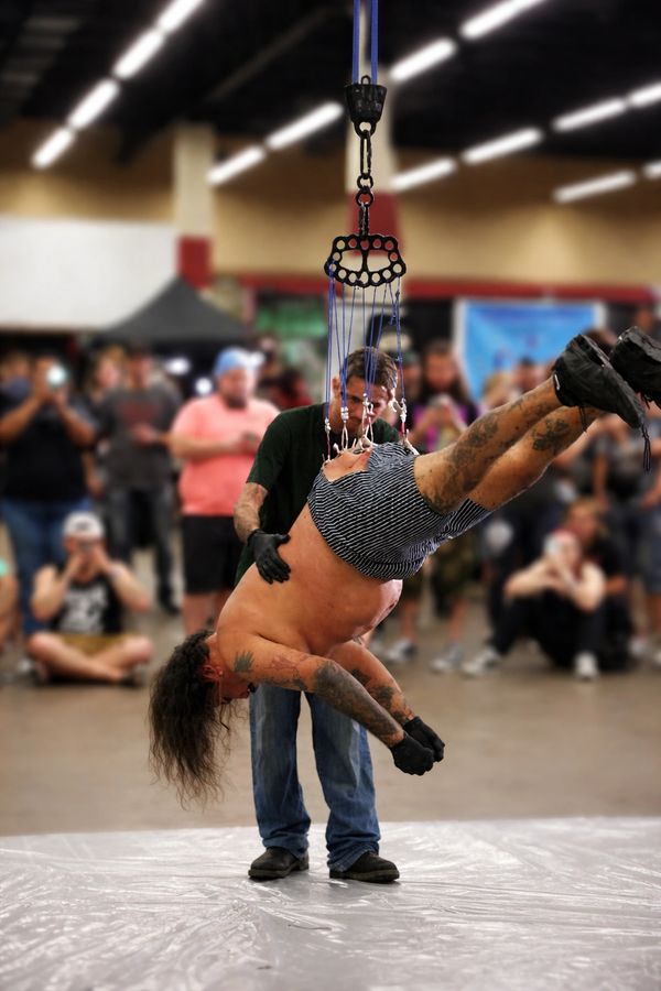 Man suspended by hooks piercing his back in front of a crowd.