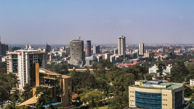 City skyline with tall buildings and greenery under a clear blue sky.