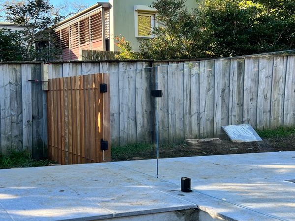 Close up of frameless glass pool fence with timber batten and copper pipe panel.