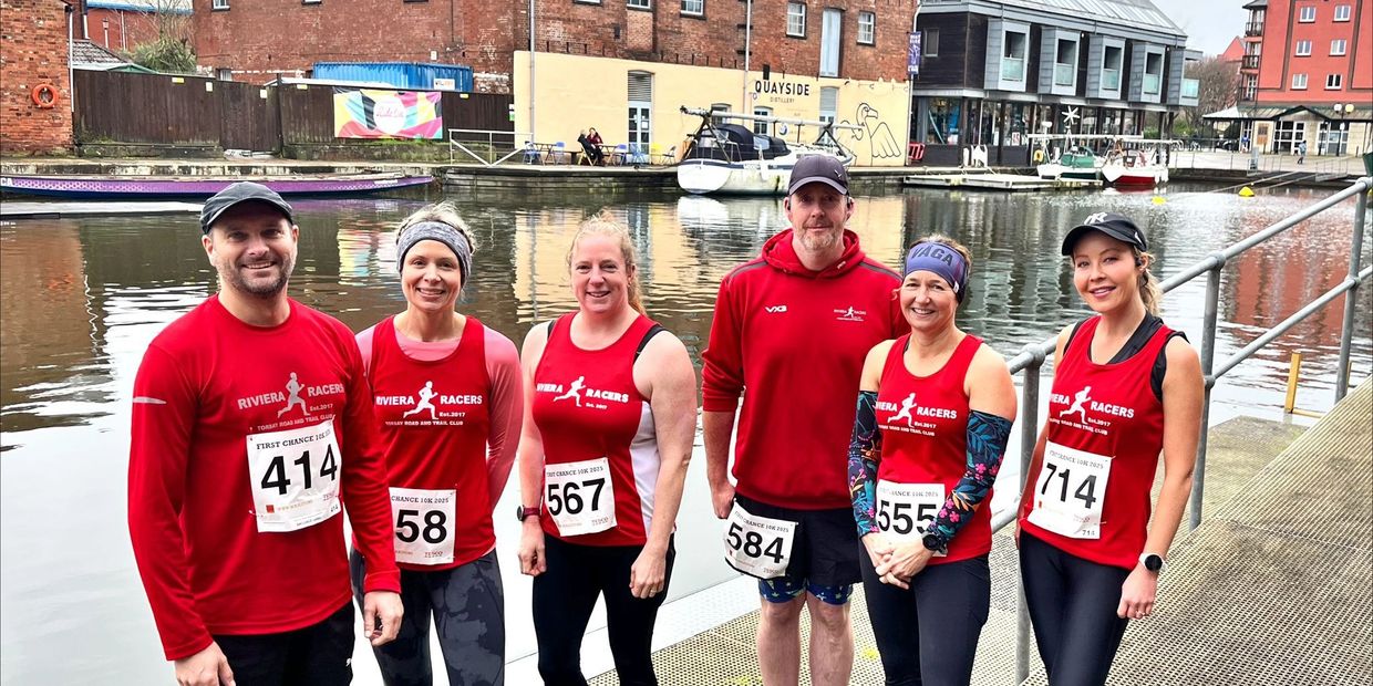 Group of six runners in red Riviera Racers shirts posing by the canal.
