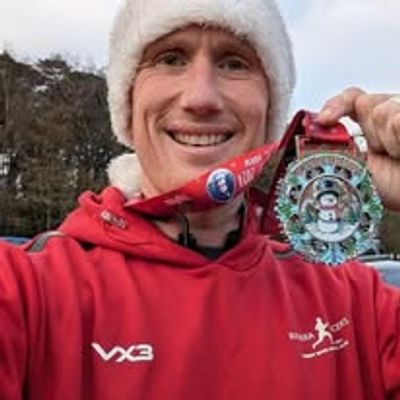 Smiling man in Santa hat holding a festive medal.