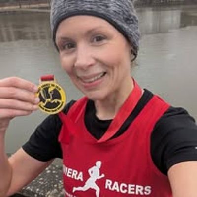 Woman in running gear holding a race medal and smiling.