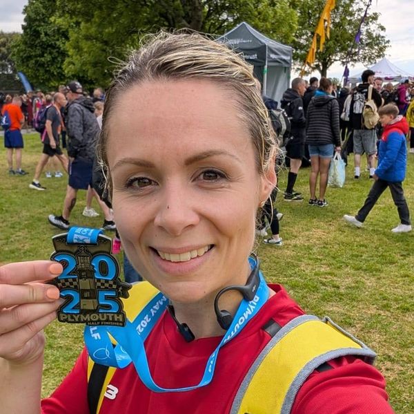Woman proudly holding a 2025 Plymouth half marathon finisher medal.