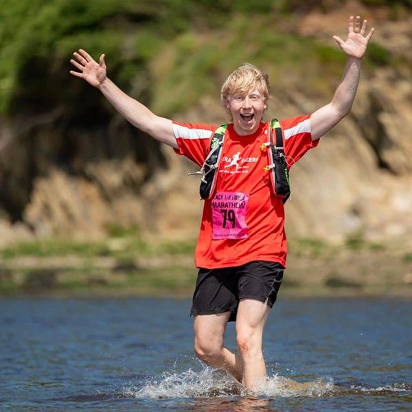 Runner in red shirt joyfully crossing shallow water with arms raised.
