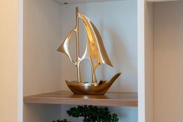 Sleek golden sailboat sculpture on a wooden shelf.