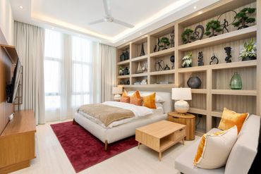 Bright modern bedroom with beige bed, orange pillows, wooden shelves, and red rug.