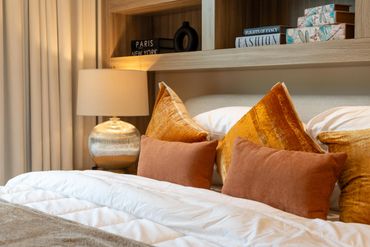 Cozy bed with orange pillows, a warm lamp, and decorative books on a wooden shelf.