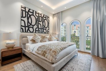 Modern bedroom with beige tones, abstract art, and large arched windows.