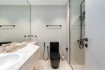 Modern bathroom with black toilet and beige marble countertop.