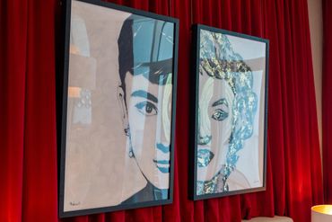 Two framed portraits with blue and gold accents against a red curtain backdrop.