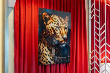 Vibrant leopard portrait mounted on red velvet curtains with a decorative white panel.