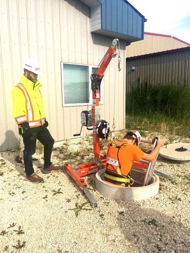 Two workers performing a confined space entry using safety equipment.