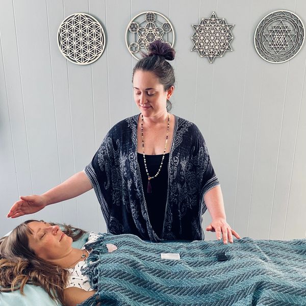 Woman giving energy healing to another woman lying down.