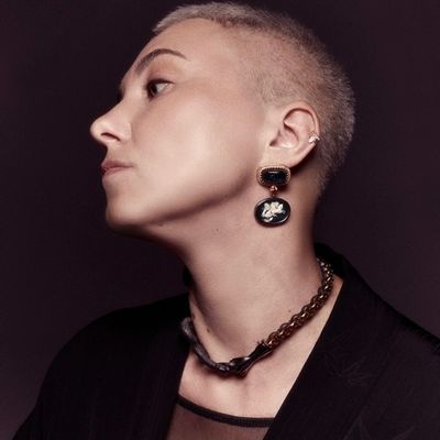 Profile of a person with a buzz cut wearing a bold earring and necklace.