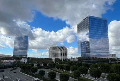 Three modern buildings under a partly cloudy sky with reflections on the glass surfaces.