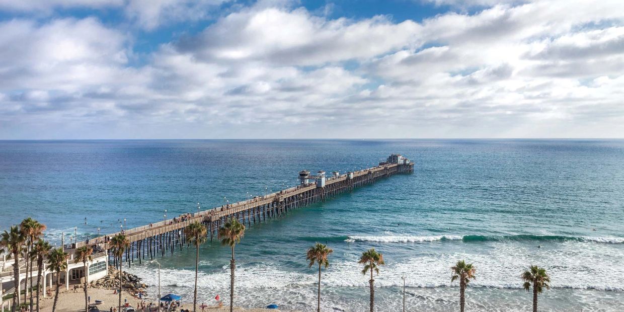 Long wooden pier extending into the ocean under a cloudy sky.